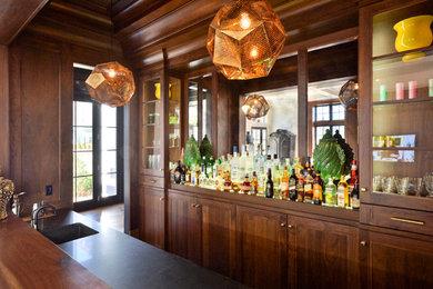 Example of a mid-sized classic galley medium tone wood floor wet bar design in New York with an integrated sink, shaker cabinets, medium tone wood cabinets, wood countertops and mirror backsplash