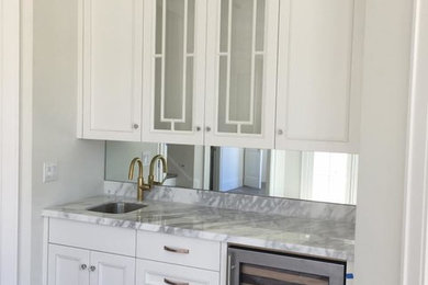 Foto på en mellanstor vintage grå u-formad hemmabar med vask, med en undermonterad diskho, luckor med infälld panel, vita skåp, marmorbänkskiva, vitt stänkskydd, spegel som stänkskydd, mörkt trägolv och brunt golv