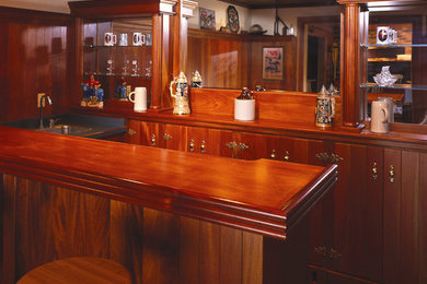 Seated home bar - small craftsman galley medium tone wood floor and brown floor seated home bar idea in Minneapolis with a drop-in sink, flat-panel cabinets, medium tone wood cabinets, wood countertops, brown backsplash and brown countertops
