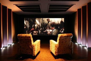 Medium sized contemporary enclosed home cinema in Berkshire with black walls, dark hardwood flooring and a projector screen.