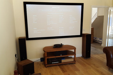 Small modern enclosed home cinema in Cambridgeshire with yellow walls, dark hardwood flooring and a projector screen.