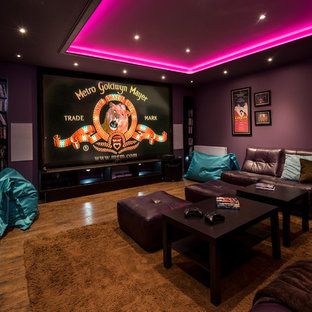 Medium sized traditional enclosed home cinema in Other with purple walls, medium hardwood flooring, a projector screen and brown floors.