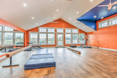 Imagen de gimnasio multiusos actual grande con parades naranjas y suelo de madera en tonos medios
