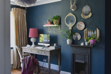 This is an example of a medium sized eclectic study in London with blue walls, dark hardwood flooring, a standard fireplace, a metal fireplace surround, a freestanding desk and brown floors.