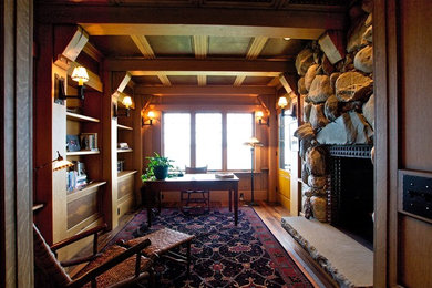 他の地域にあるお手頃価格の広いラスティックスタイルのおしゃれな書斎 (茶色い壁、無垢フローリング、標準型暖炉、石材の暖炉まわり、自立型机) の写真