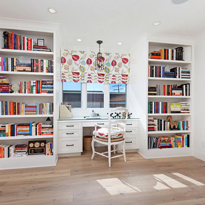 Large transitional built-in desk medium tone wood floor home office library photo in Orange County with white walls