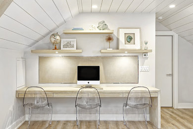 Diseño de despacho costero sin chimenea con paredes blancas, suelo de madera clara y escritorio empotrado