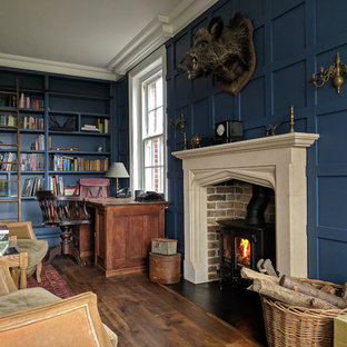 Inspiration för mellanstora klassiska hemmabibliotek, med blå väggar, mellanmörkt trägolv, en öppen vedspis, ett fristående skrivbord, brunt golv och en spiselkrans i tegelsten