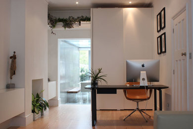 This is an example of a medium sized modern home office in London with medium hardwood flooring.