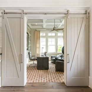Maritimes Arbeitszimmer mit weißer Wandfarbe, Backsteinboden, freistehendem Schreibtisch und rotem Boden in Charleston