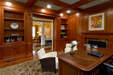 Diseño de despacho clásico de tamaño medio con biblioteca, suelo de madera en tonos medios, todas las chimeneas, marco de chimenea de piedra y escritorio independiente
