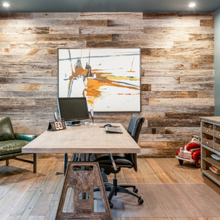 Klassisches Arbeitszimmer ohne Kamin mit Arbeitsplatz, grauer Wandfarbe, braunem Holzboden, freistehendem Schreibtisch, braunem Boden und Holzwänden in Sonstige