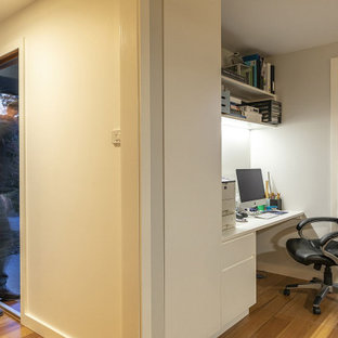 Modern inredning av ett litet hemmabibliotek, med vita väggar, bambugolv och ett inbyggt skrivbord