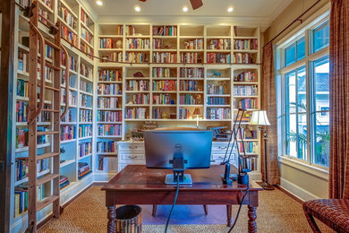 Imagen de despacho tropical con biblioteca, suelo de madera en tonos medios y escritorio independiente