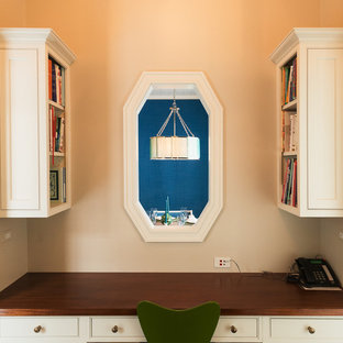 Exemple d'un grand bureau chic de type studio avec un mur beige, un sol en bois brun, une cheminée standard et un manteau de cheminée en pierre.