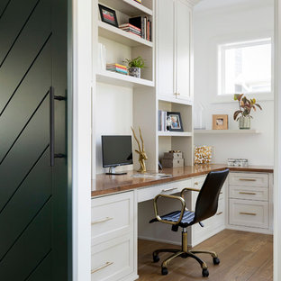 Maritim inredning av ett mellanstort hemmastudio, med vita väggar, mellanmörkt trägolv, ett inbyggt skrivbord och beiget golv