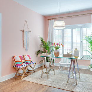 Exotisk inredning av ett mellanstort hemmabibliotek, med rosa väggar, mellanmörkt trägolv, ett fristående skrivbord och brunt golv