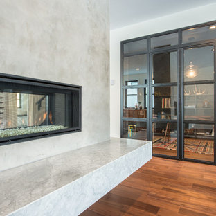 Cette image montre un bureau design avec un mur noir, un sol en bois brun, une cheminée double-face, un manteau de cheminée en béton et un bureau indépendant.