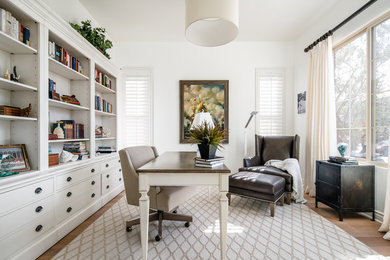 Modelo de despacho clásico renovado grande con paredes blancas, suelo de madera clara, escritorio independiente y suelo beige
