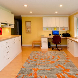 Aménagement d'un grand bureau contemporain de type studio avec un mur jaune, un sol en bois clair et un bureau intégré.
