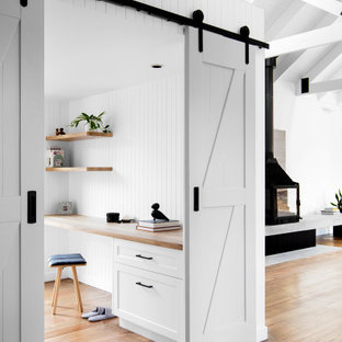 Inspiration för ett litet funkis hemmabibliotek, med vita väggar, mellanmörkt trägolv, en öppen vedspis, en spiselkrans i betong och ett inbyggt skrivbord