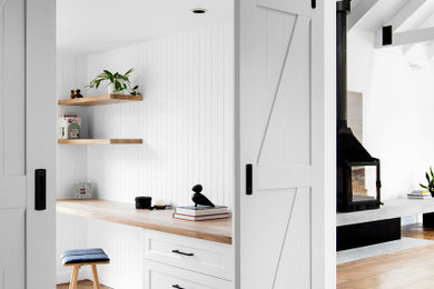 Imagen de despacho abovedado actual pequeño con paredes blancas, suelo de madera en tonos medios, estufa de leña, marco de chimenea de hormigón, escritorio empotrado y panelado