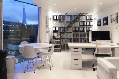 Foto på ett litet funkis hemmastudio, med vita väggar, ljust trägolv, en öppen vedspis och ett fristående skrivbord