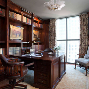 Klassisches Arbeitszimmer mit brauner Wandfarbe, dunklem Holzboden, Einbau-Schreibtisch, braunem Boden, Wandpaneelen und Holzwänden in Austin