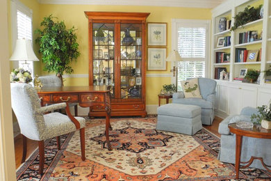 Diseño de despacho clásico de tamaño medio con paredes amarillas, suelo de madera en tonos medios y escritorio independiente