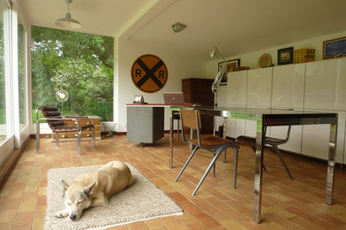 Imagen de estudio minimalista pequeño con paredes blancas, suelo de baldosas de terracota y escritorio independiente