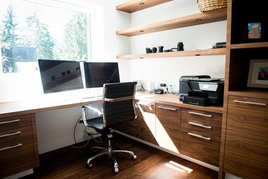 Modelo de despacho actual de tamaño medio con paredes blancas, suelo de madera en tonos medios y escritorio empotrado