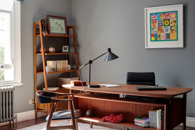 Mittelgroßes Mid-Century Arbeitszimmer mit Arbeitsplatz, grauer Wandfarbe, dunklem Holzboden und freistehendem Schreibtisch in London