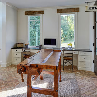 Aménagement d'un grand bureau campagne de type studio avec un mur blanc, un sol en brique, aucune cheminée, un bureau intégré et un sol beige.