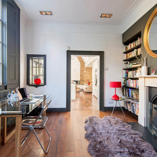 This is an example of a contemporary study in London with grey walls, medium hardwood flooring, a standard fireplace, a freestanding desk and brown floors.
