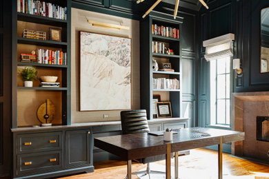 Diseño de despacho abovedado clásico renovado de tamaño medio con paredes verdes, suelo de madera en tonos medios, todas las chimeneas, marco de chimenea de piedra, escritorio independiente, suelo marrón y panelado