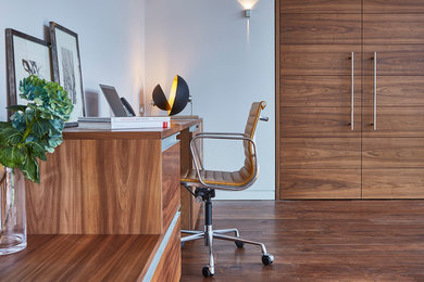 Cette image montre un bureau design avec un mur blanc, un sol en bois brun et un bureau intégré.