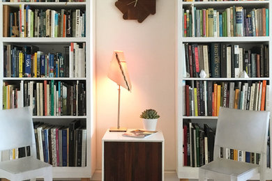Inredning av ett modernt litet arbetsrum, med ett bibliotek, vita väggar, mellanmörkt trägolv, ett fristående skrivbord och brunt golv