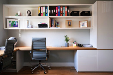Идея дизайна: большое рабочее место в современном стиле с серыми стенами, паркетным полом среднего тона, встроенным рабочим столом и коричневым полом