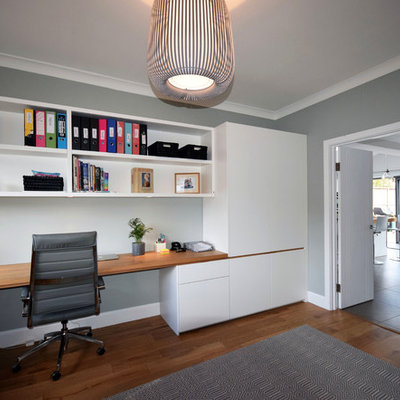 Study room - large contemporary built-in desk medium tone wood floor and brown floor study room idea in London with gray walls