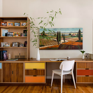 Aménagement d'un petit bureau rétro avec un mur beige, un sol en bois brun, un bureau intégré et un sol marron.