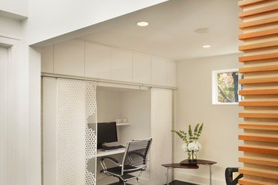 Example of a trendy built-in desk dark wood floor home office design in DC Metro with white walls