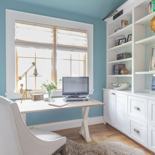 Großes Landhaus Arbeitszimmer ohne Kamin mit blauer Wandfarbe, hellem Holzboden, freistehendem Schreibtisch und beigem Boden in Houston