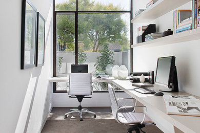 Diseño de despacho actual sin chimenea con paredes blancas, suelo de cemento y escritorio empotrado