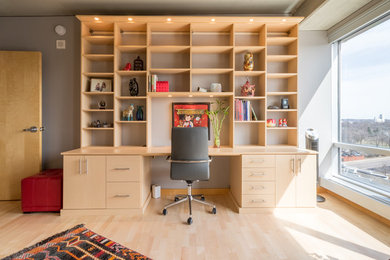Diseño de despacho contemporáneo grande con paredes grises, suelo de madera clara y escritorio empotrado