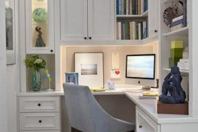 Modelo de despacho clásico de tamaño medio sin chimenea con paredes blancas, suelo de madera en tonos medios, escritorio empotrado y suelo marrón