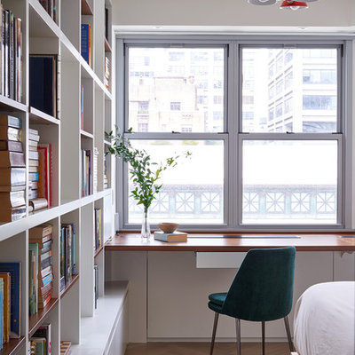 Trendy built-in desk light wood floor and beige floor home office library photo in New York with white walls