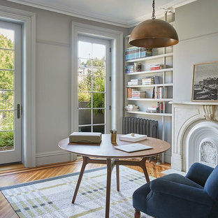 Inspiration för ett stort vintage arbetsrum, med ett bibliotek, grå väggar, ljust trägolv, en standard öppen spis, en spiselkrans i betong, ett fristående skrivbord och brunt golv