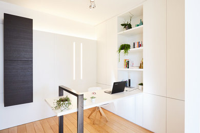 Modelo de despacho minimalista con paredes blancas, suelo de madera en tonos medios y escritorio empotrado