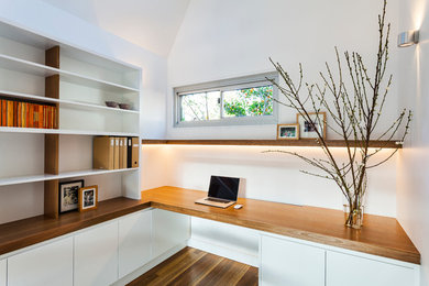 Bild på ett litet funkis hemmabibliotek, med vita väggar, mellanmörkt trägolv och ett inbyggt skrivbord