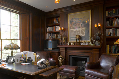 ロンドンにあるラグジュアリーな中くらいなトラディショナルスタイルのおしゃれな書斎 (茶色い壁、濃色無垢フローリング、標準型暖炉、塗装板張りの暖炉まわり、自立型机、茶色い床、板張り壁) の写真